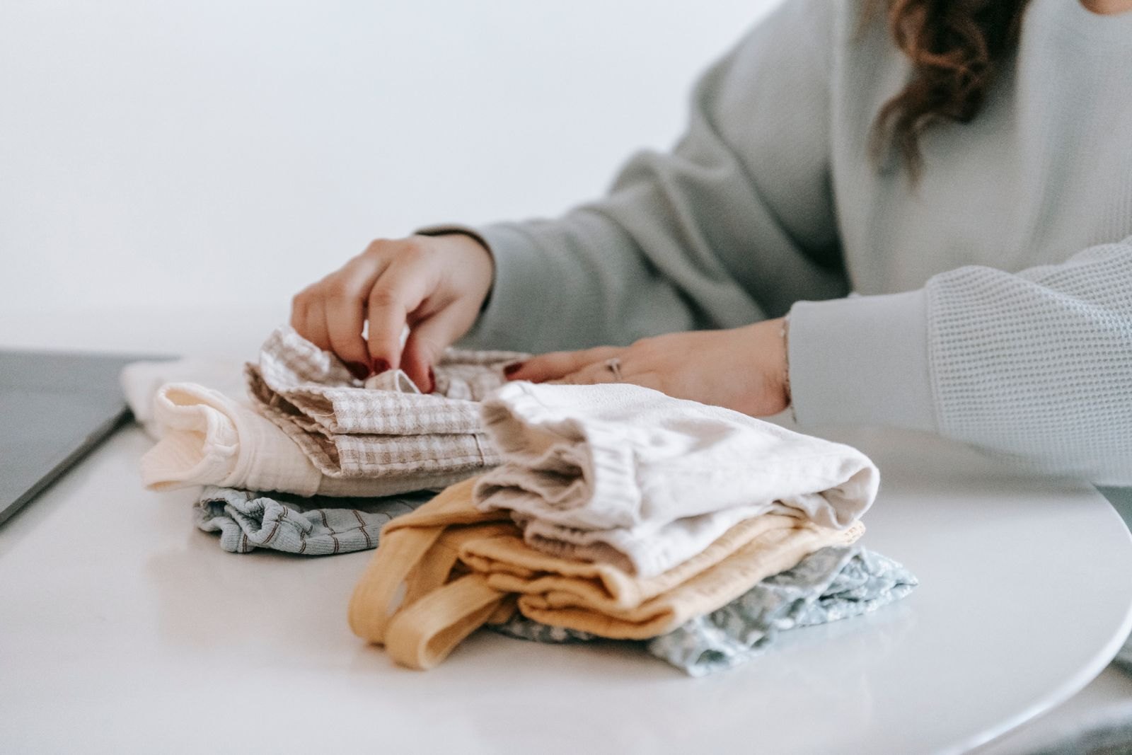 Hands arranging folded baby clothes on a table
