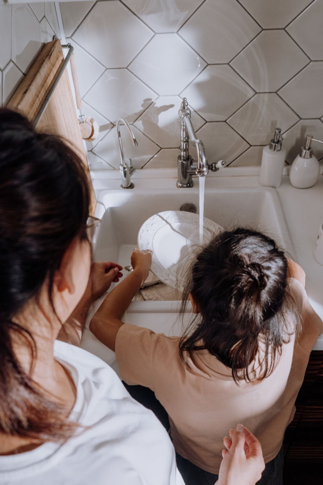 Child washing dishes with an adult nearby