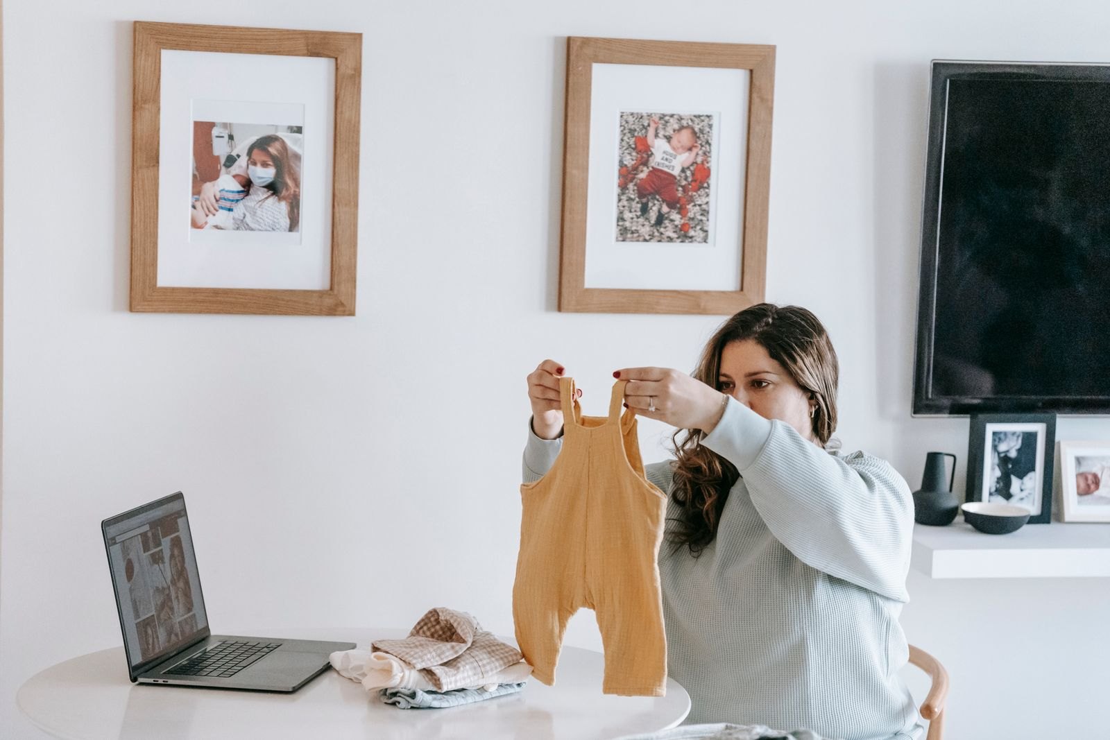 Young woman folding baby clothes sitting near table at home