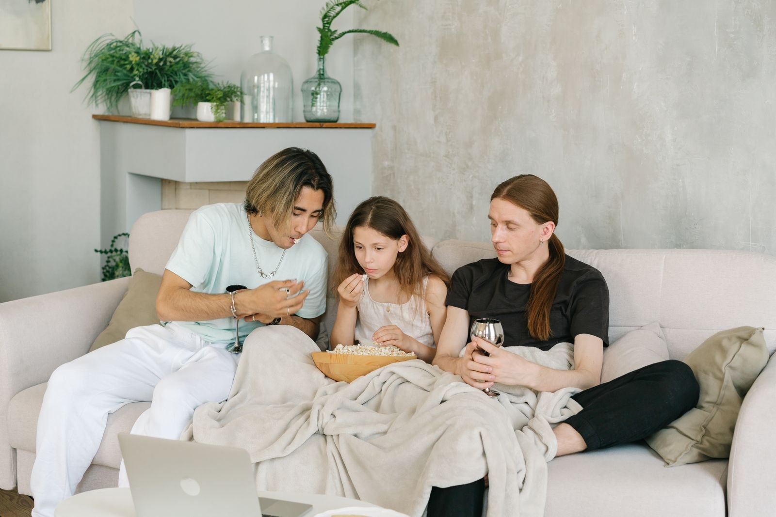 A family watching a movie while eating popcorn on a couch