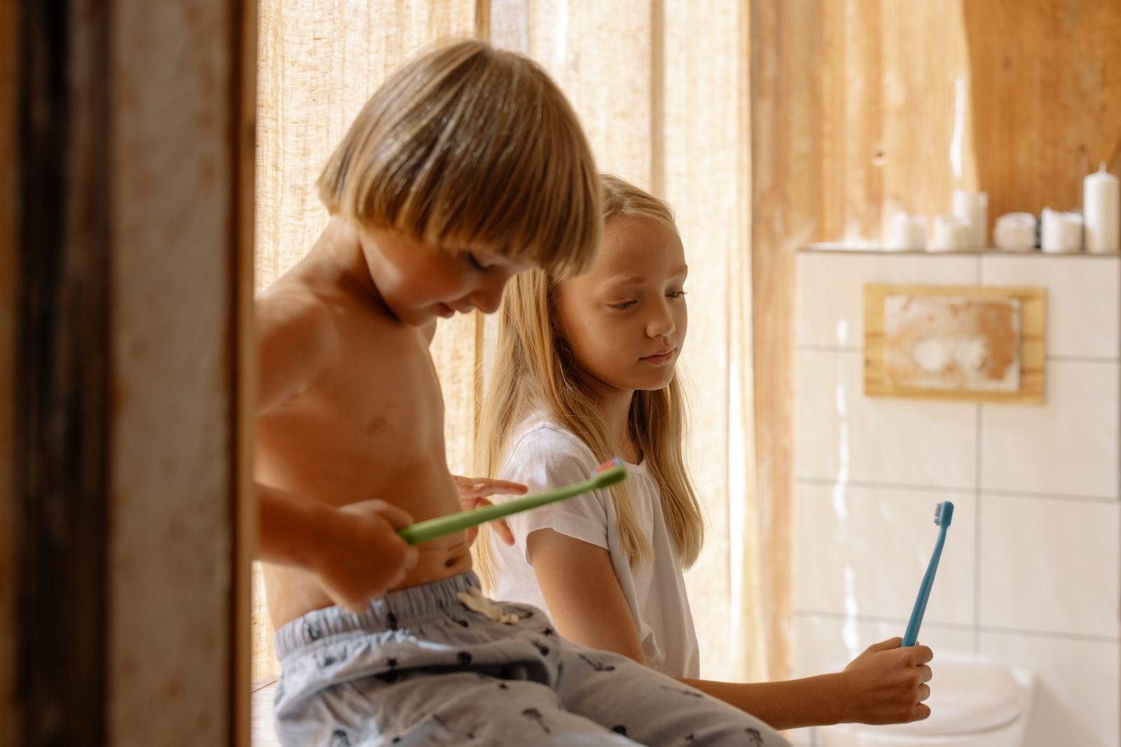 Brother and sister holding their toothbrushes inside the bathroom